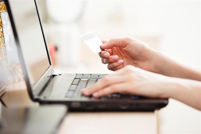 Closeup of woman holding credit card and using laptop