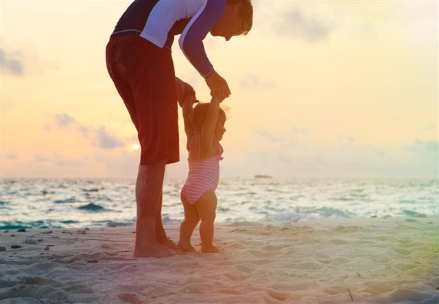 Father and little daughter walking on sunset beach