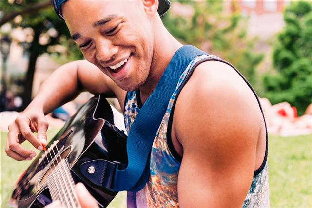 Smiling Young Black Man Playing Acoustic Guitar in NYC Park