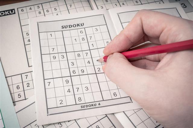 Hand holding pencil is solving sudoku crossword