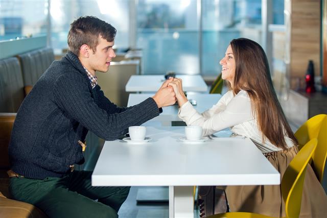 Happy couple sitting in cafe holding hands