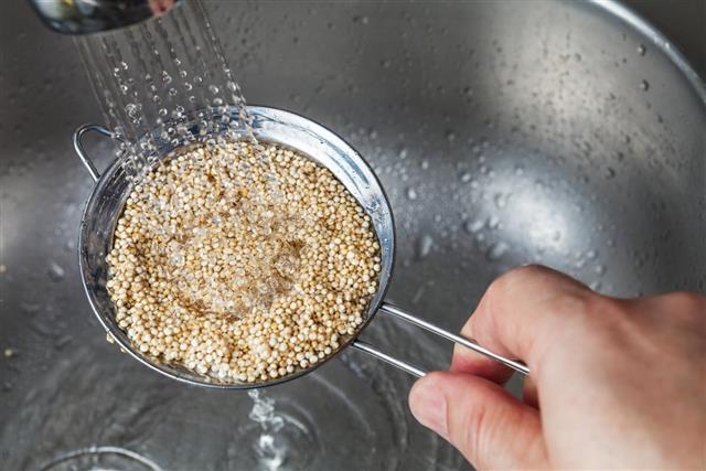 Man holding small strainer with raw quinoa seeds