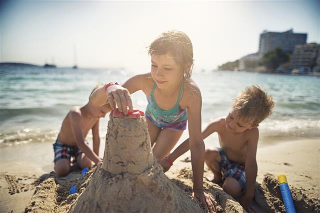 Brothers and sister building a sandcastle on beautiful beach