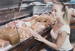 Woman customer buying fresh chicken parts in meat shop