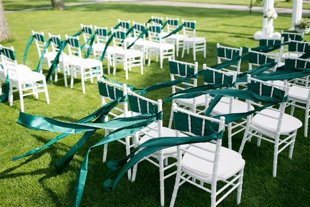 White wedding chairs with green and emerald ribbon outdoors