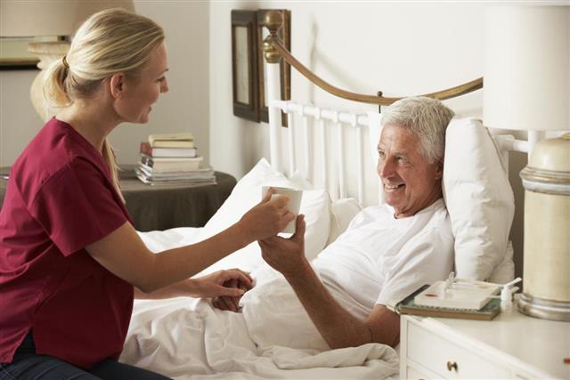 Health Visitor Giving Senior Male Hot Drink In Bed