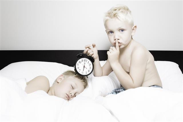 Little Boy Holding Alarm Clock to Sleeping Brother