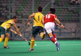 Three players playing hockey on a pitch