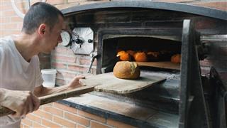 Baker checking a bread loaf in a traditional stove