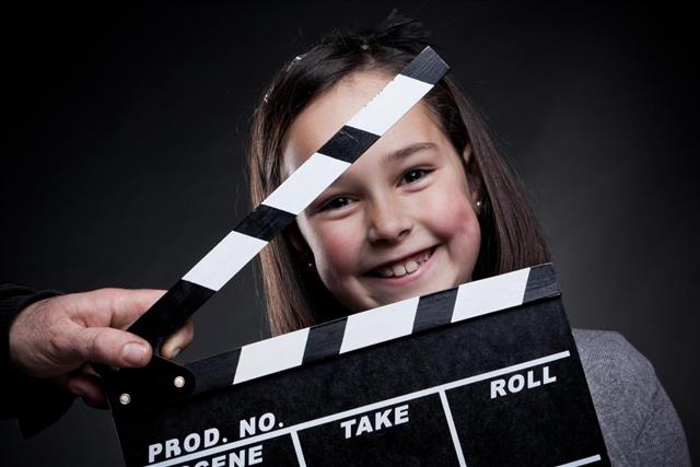 Portrait of smiling young girl behind a movie clapper board