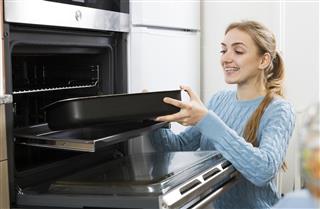 girl putting baking tray in kitchen oven