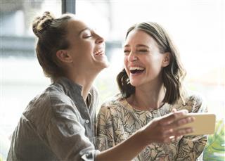 Woman holding mobile phone with friend and laughing