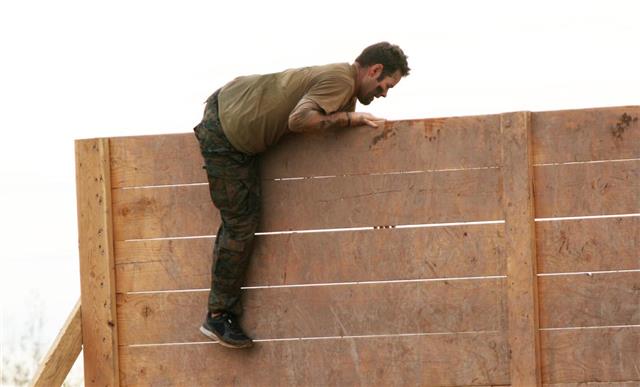 Man climbs wall obstacle at a mud run obstacle course event