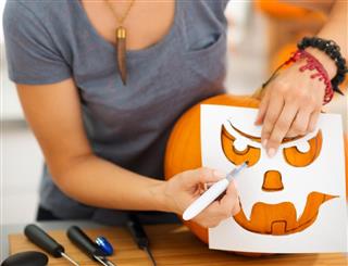 Happy young woman using stencils to carve pumpkin