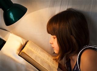 Girl reading book on bed at night