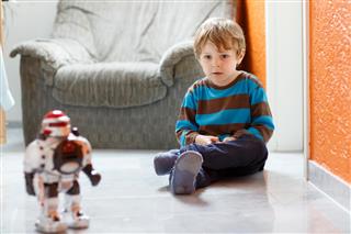 Little blond boy playing with robot toy at home, indoor.