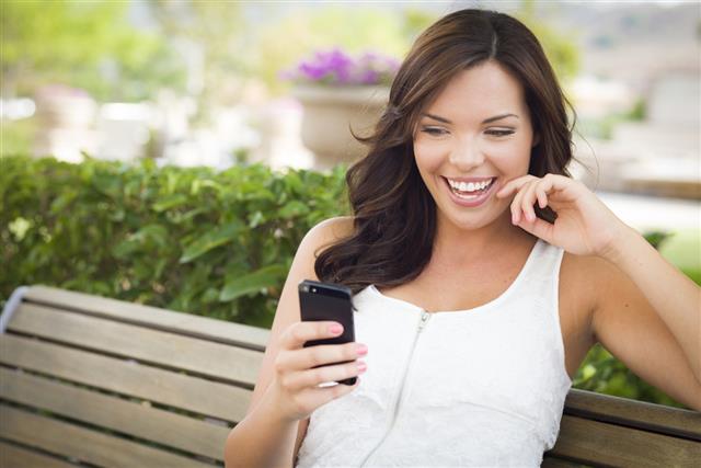 Smiling woman looking at smartphone while seated on bench