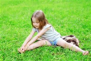 Little girl child sitting on the grass does yoga stretching