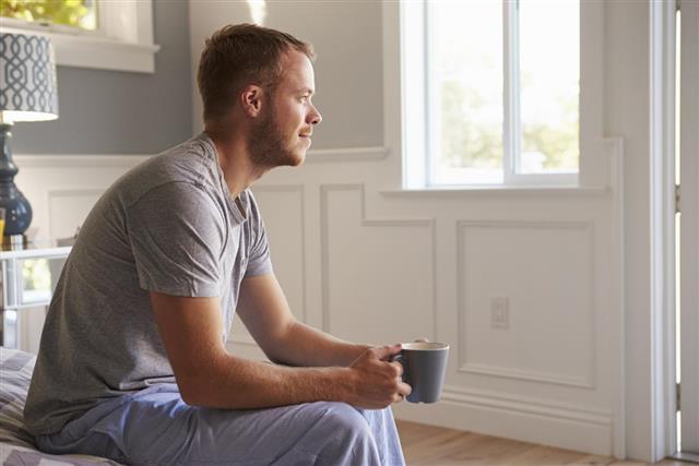 Man Wearing Pajamas Sitting On Bed With Hot Drink