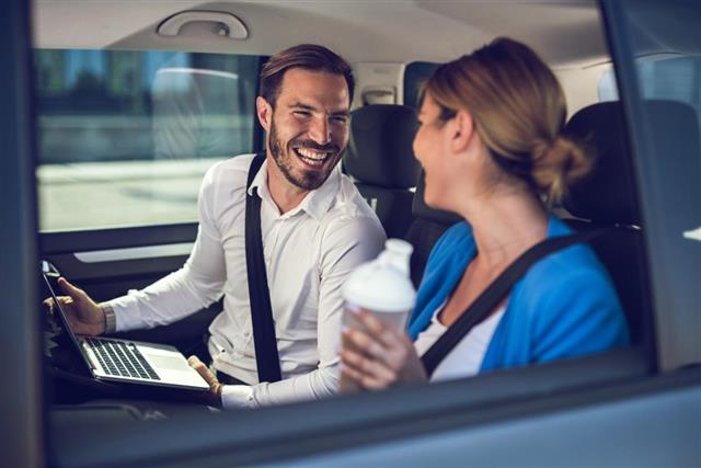Happy businessman talking to his female colleague in the car.