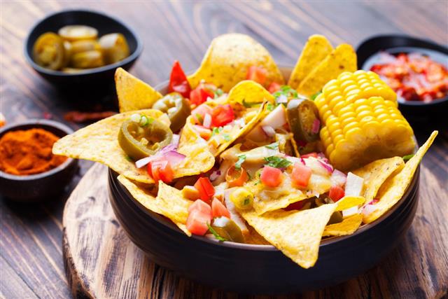 Nachos with melted cheese sauce, salsa, corn cobs in bowl