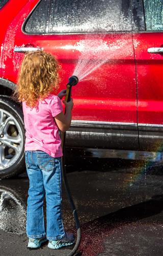Girl Washing Red Vehicle With Garden Hose