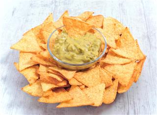 Bowl of guacamole sauce surrounded by nachos