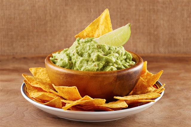 Mexican nacho chips with guacamole in a bowl and a lime
