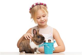 Smiling girl feeding bunny with chocolate eggs