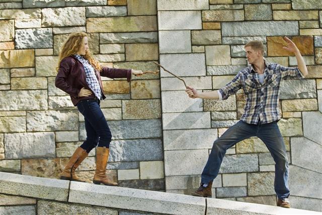 Couple play fighting with sticks against stone wall