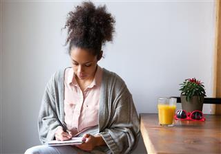 Young woman sitting at home writing on notepad
