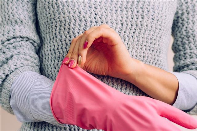 Woman in gray sweater and pink manicure wears rubber glove