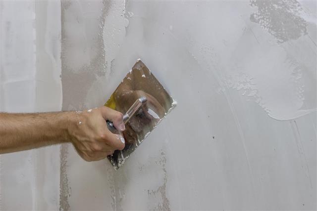 man hand with trowel plastering a wall