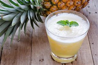 Glass of pineapple smoothie on wooden table