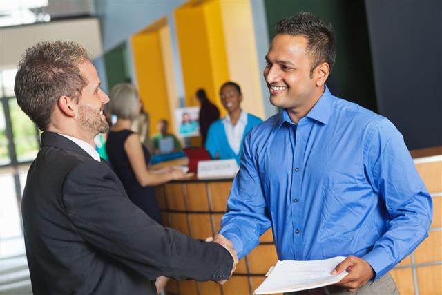 Two business men shaking hands exchanging resumes at job fair