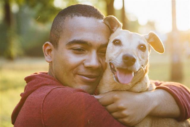 Young man hug his small Mixed-breed dog, looking at camera