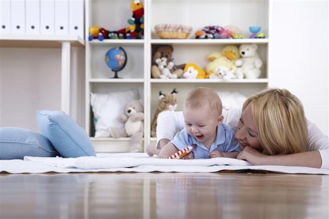 Mother lying on floor with smiling baby in playroom