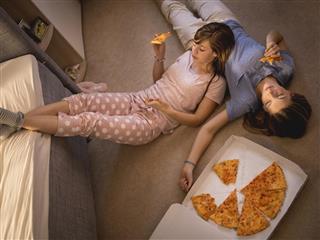 Teen girls eating pizza while lying on a bedroom floor