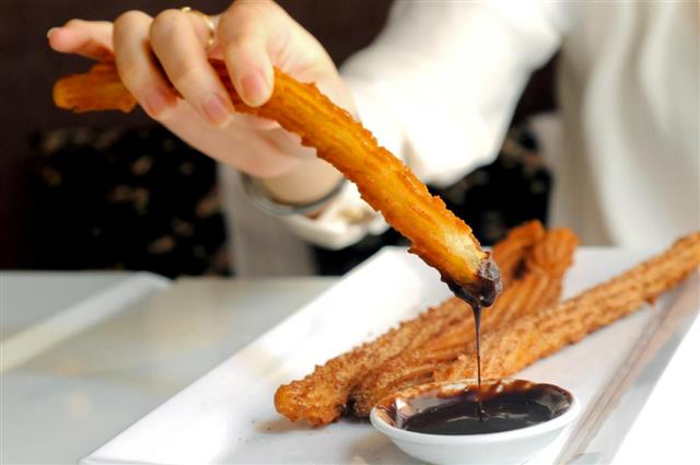 Female hand dipping Churros to chocolate sauce