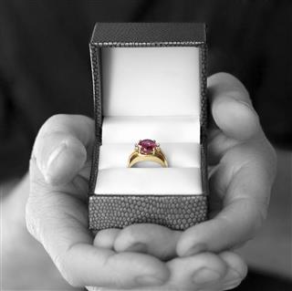 A gray scale person holding a golden and ruby ring