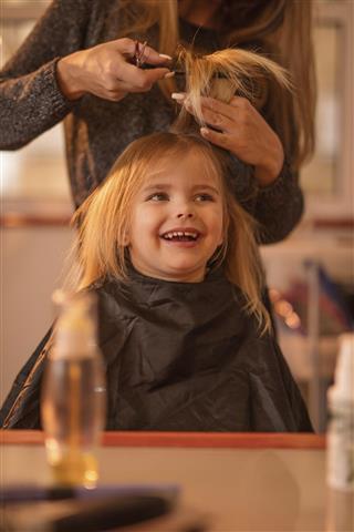 Cute little girl during hair cut at hair salon.