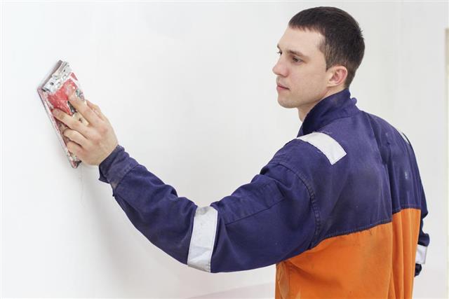 Man working with sandpaper on a white wall