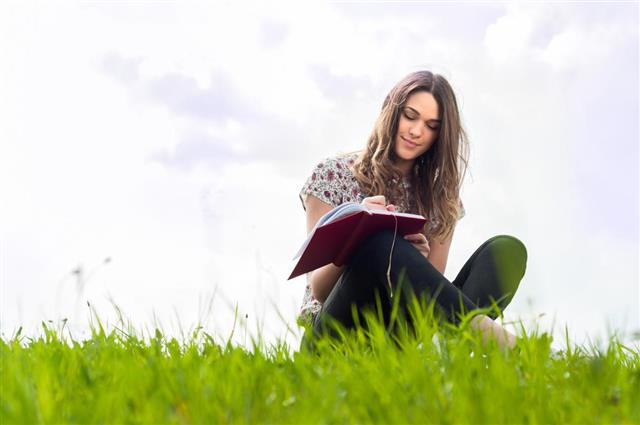 Beautiful young girl with a notebook siting down on lawn