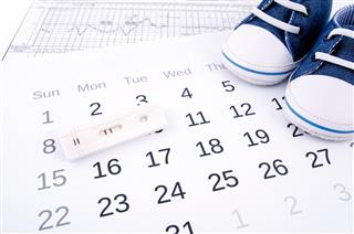 Positive pregnancy test on calendar and baby shoes
