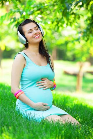 Pregnant woman with headphones in the park