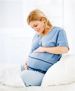 Smiling pregnant young lady sitting on bed