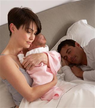 Mother Cuddling Newborn Baby In Bed At Home
