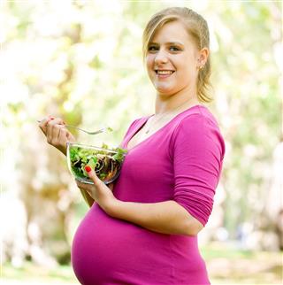Happy and young pregnant woman with food in the park