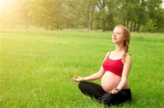  Schwangere Frau, die in der Natur, Praxis Yoga meditiert