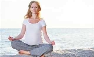 Pregnant woman practicing yoga in lotus position on beach